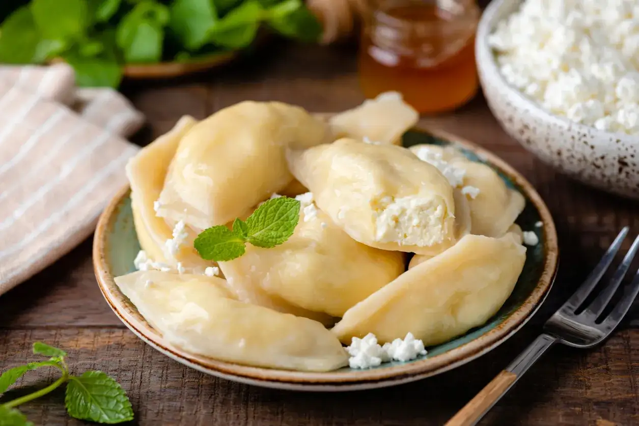 Talerz pełen pysznych, domowych pierogów z serem, udekorowanych miętą i pokruszonym twarogiem. Idealne na deser lub śniadanie.